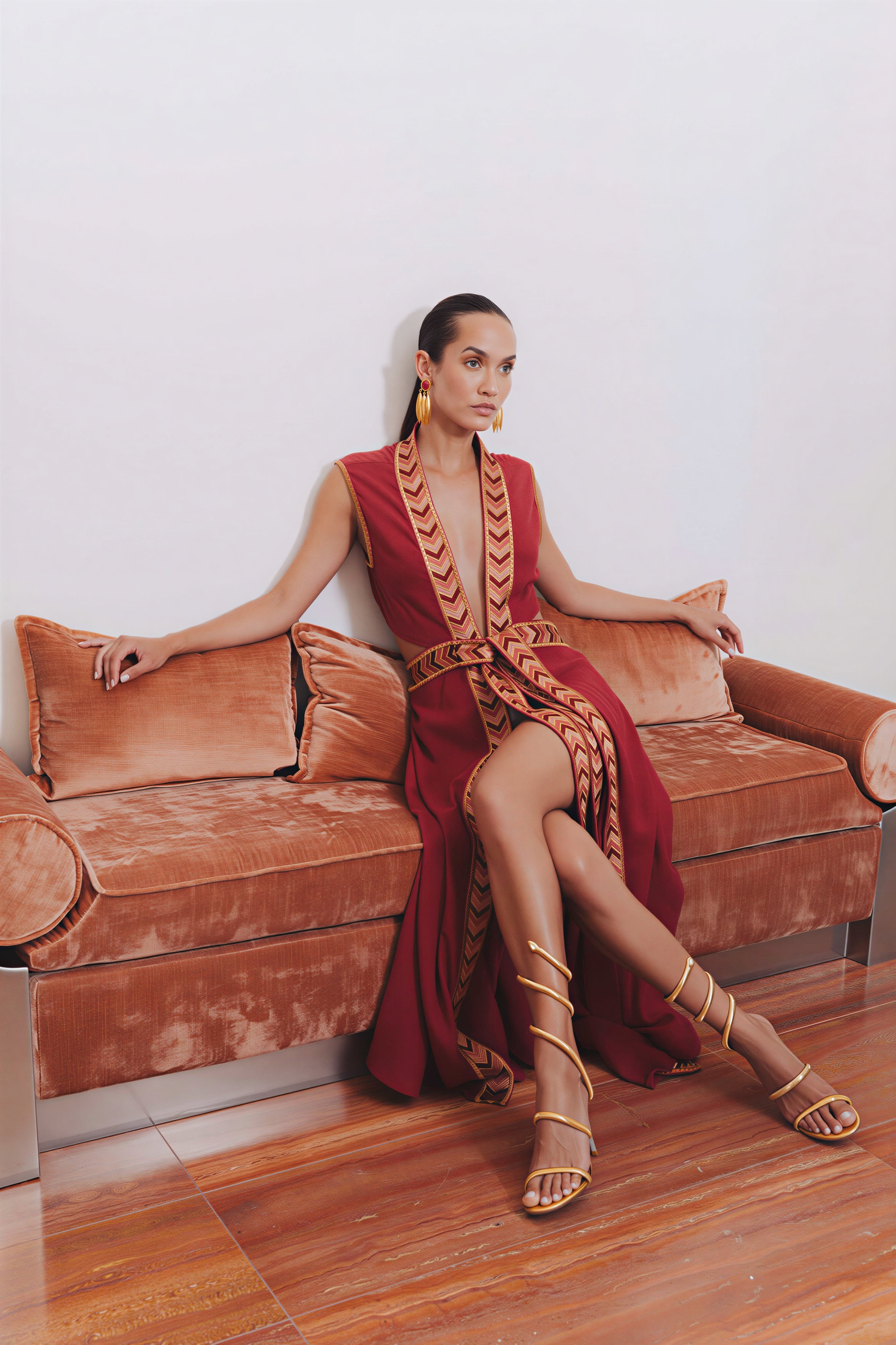 Model wearing the Natacha & Vanessa The Oceanne dress in red with metallic sandals while reclining on a velvet sofa.