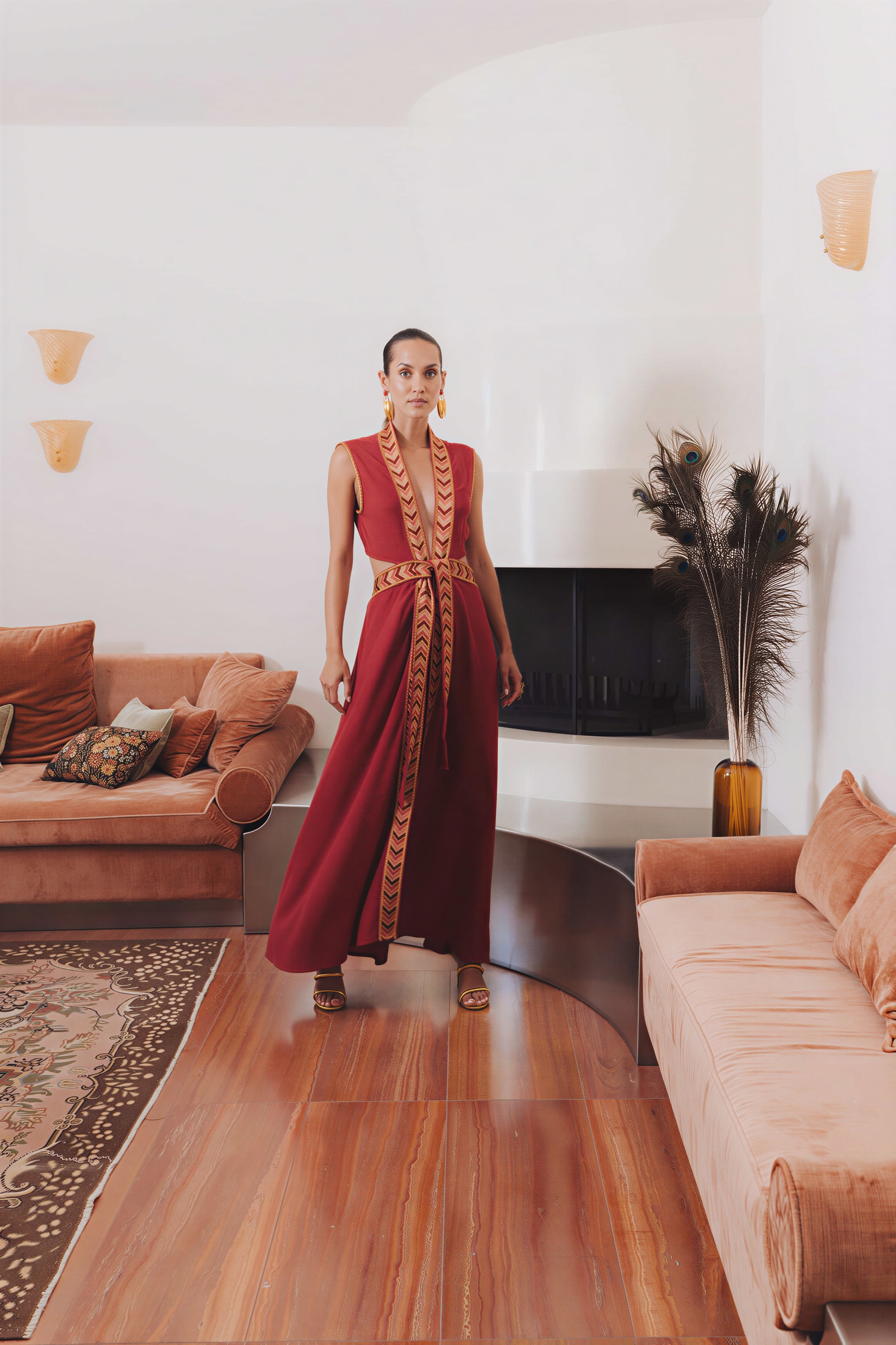Model wearing the Natacha & Vanessa The Thalie dress in red with embroidered trim and braided belt in an elegant interior.