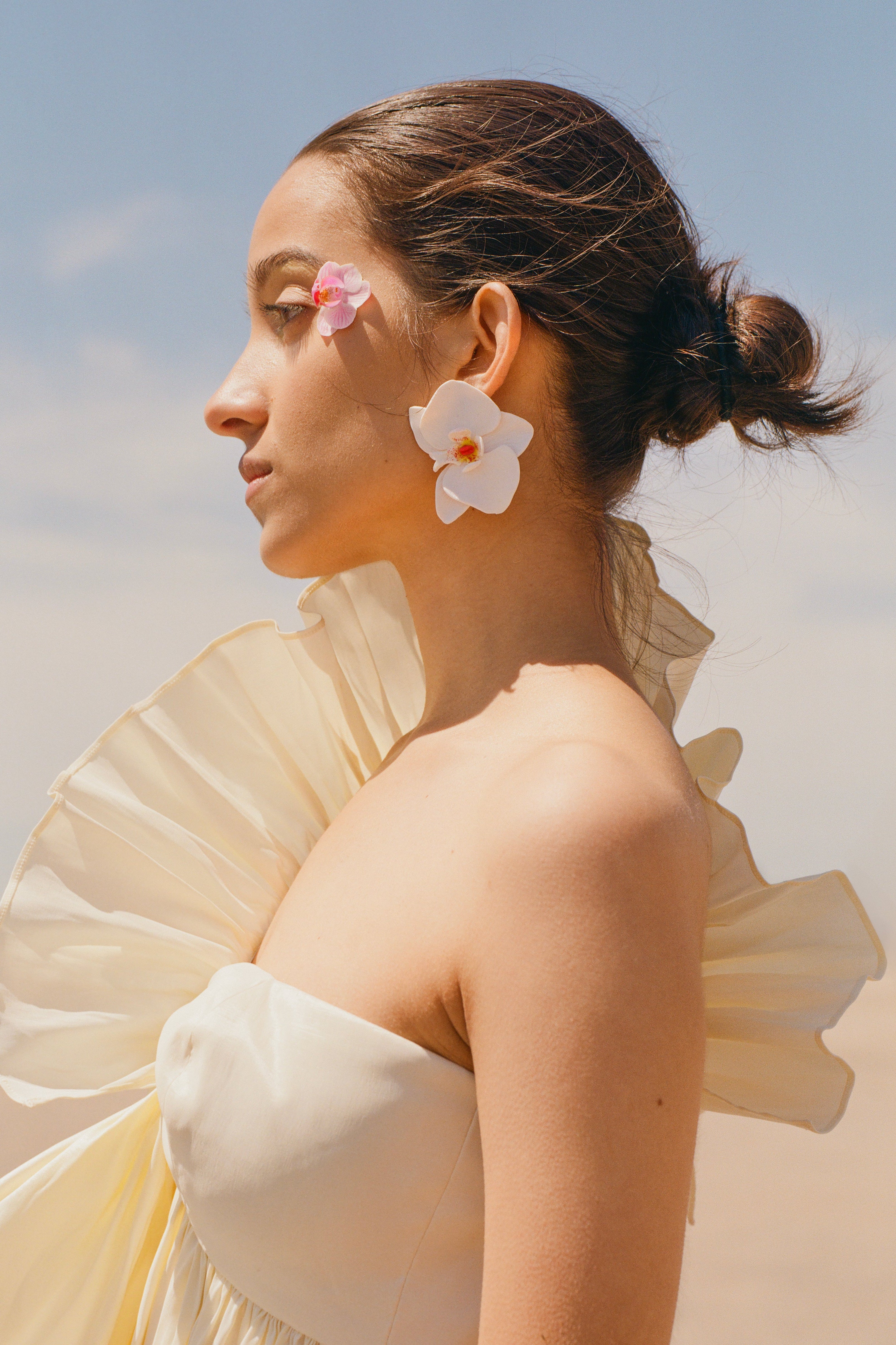  Model wearing Kenza Klay oversized white orchid statement earrings handcrafted from polymer clay with warm pink and yellow centers.