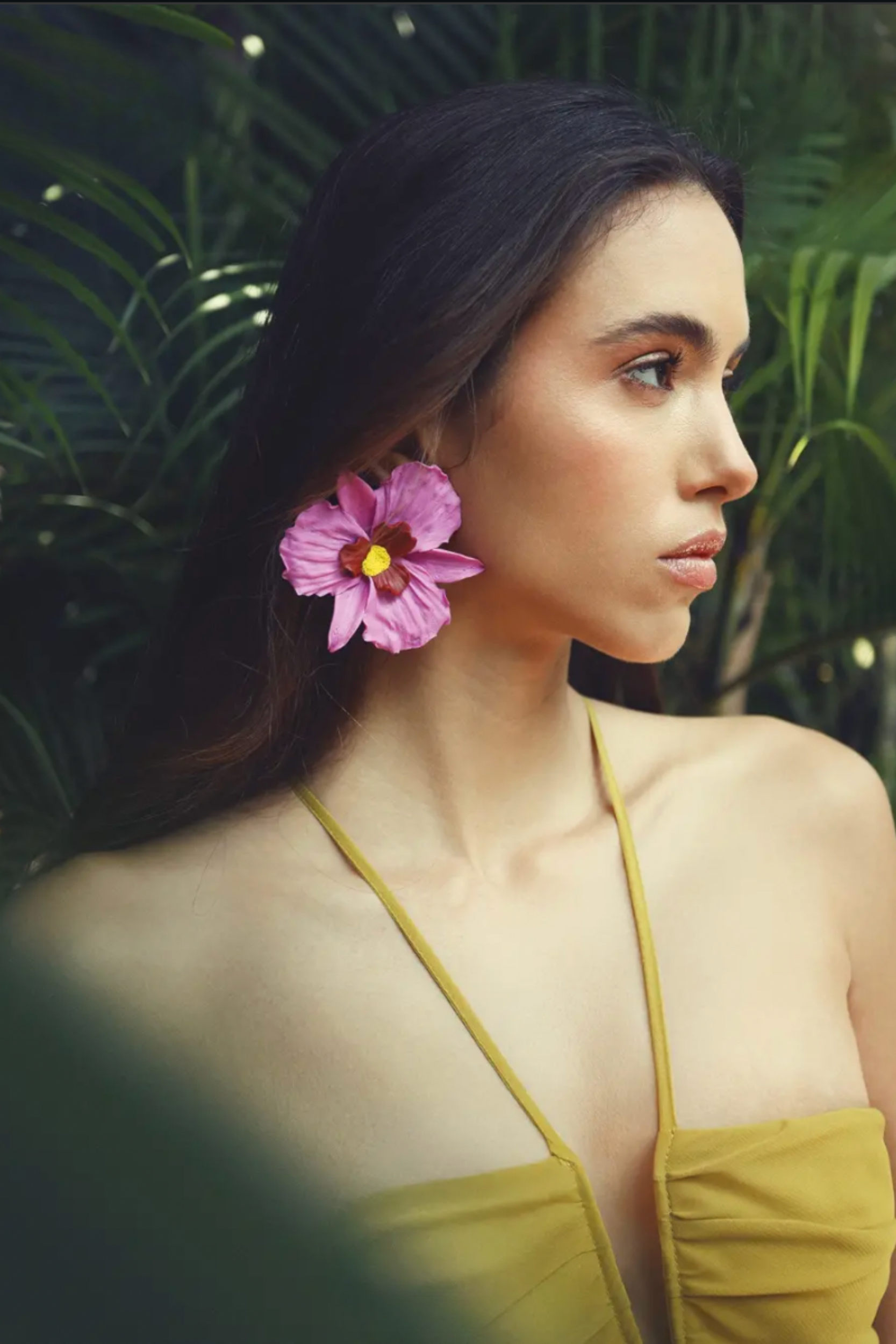 Woman wearing oversized pink orchid flower statement earrings with yellow and burgundy centers,