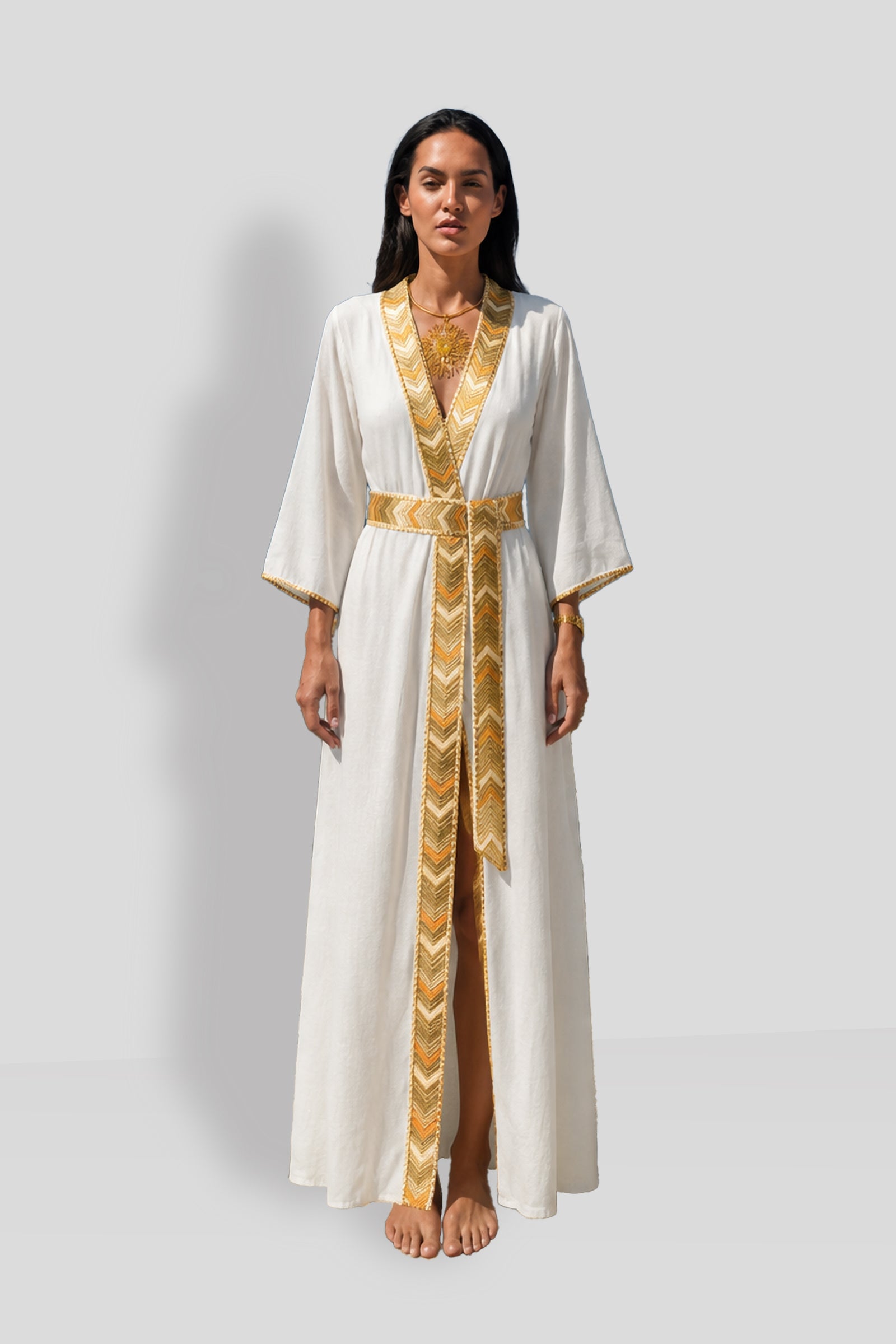Natacha & Vanessa Livia Maxi Dress in ecru featuring a deep V-neckline, ochre and gold gradient trim, long sleeves, and an integrated waist tie.