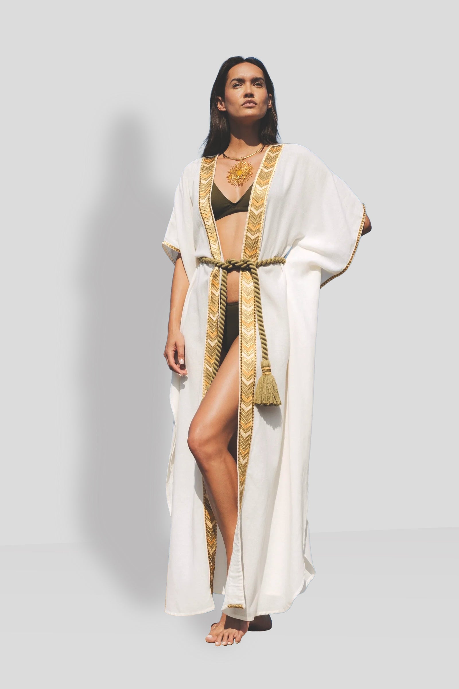 Natacha & Vanessa Ocean Dress in white featuring a deep V-neckline, gold embroidered trim, wide kimono sleeves, and a detachable braided rope belt.