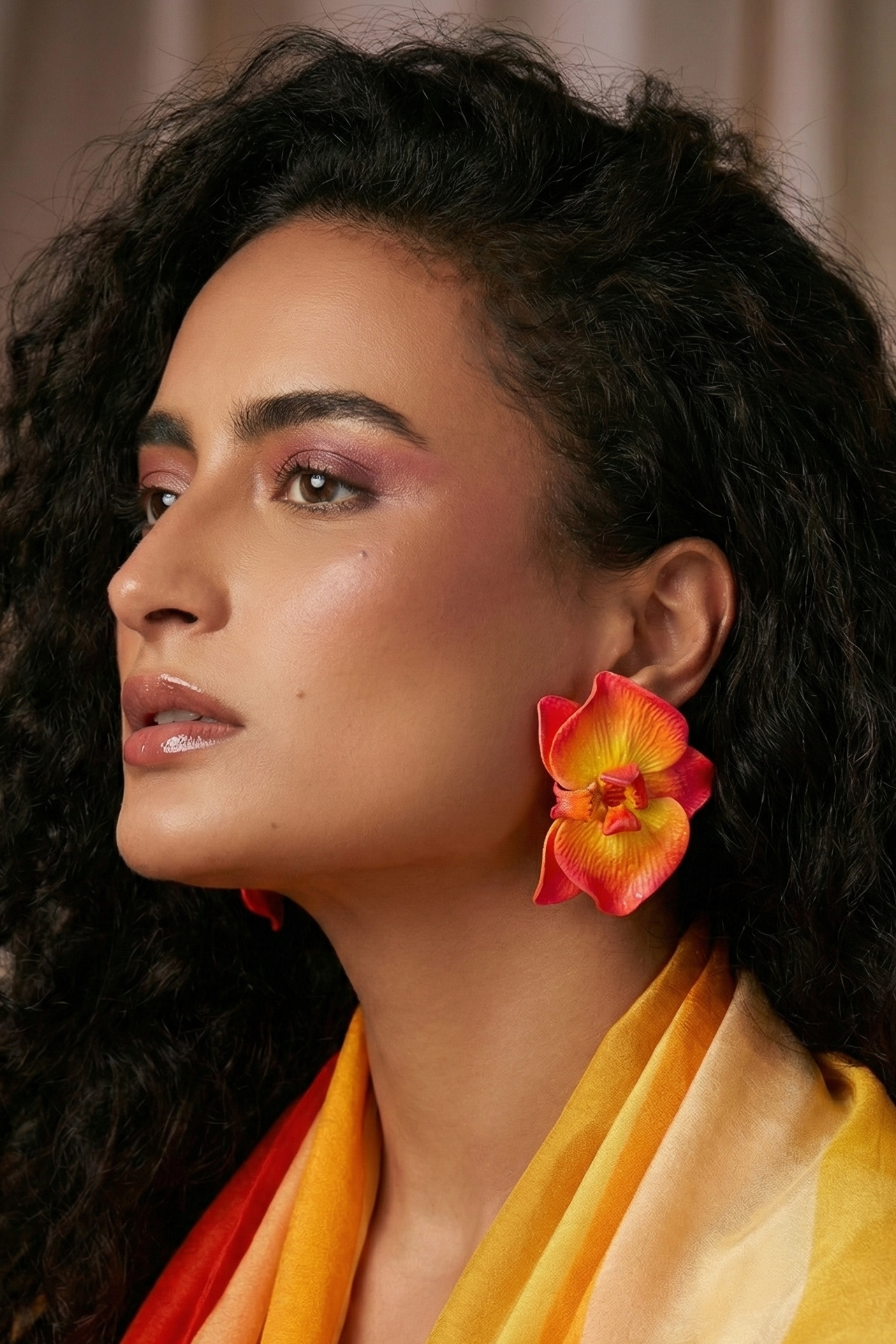 Woman wearing handcrafted Sunset Orchid Earrings in fiery sunset shades of yellow, orange, and red, bold floral statement earrings for special occasions and resort wear.