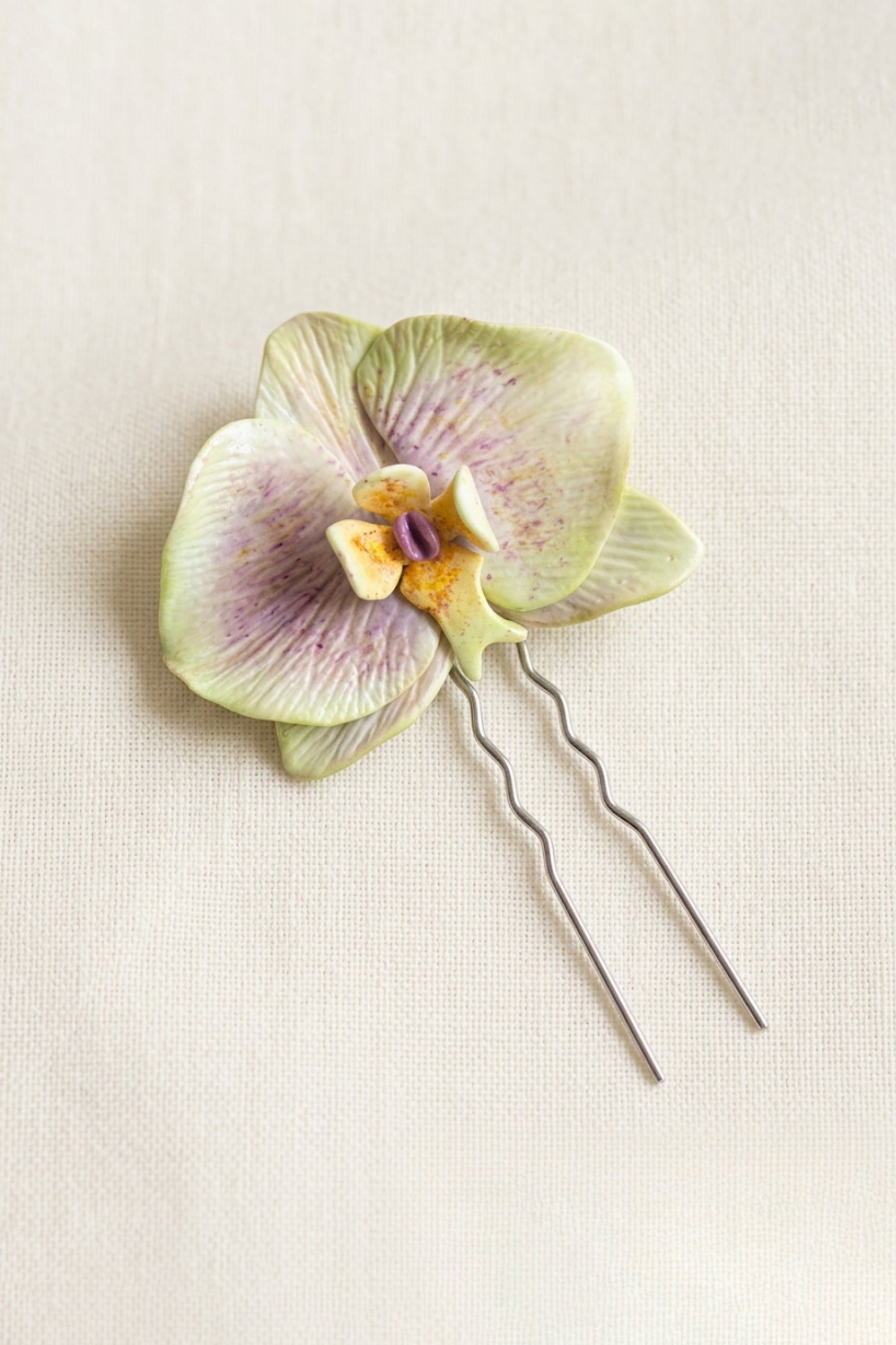 Opaline Orchid Hairpin featuring a handcrafted orchid bloom in pale green and lilac tones with a decorative hairpin attachment.