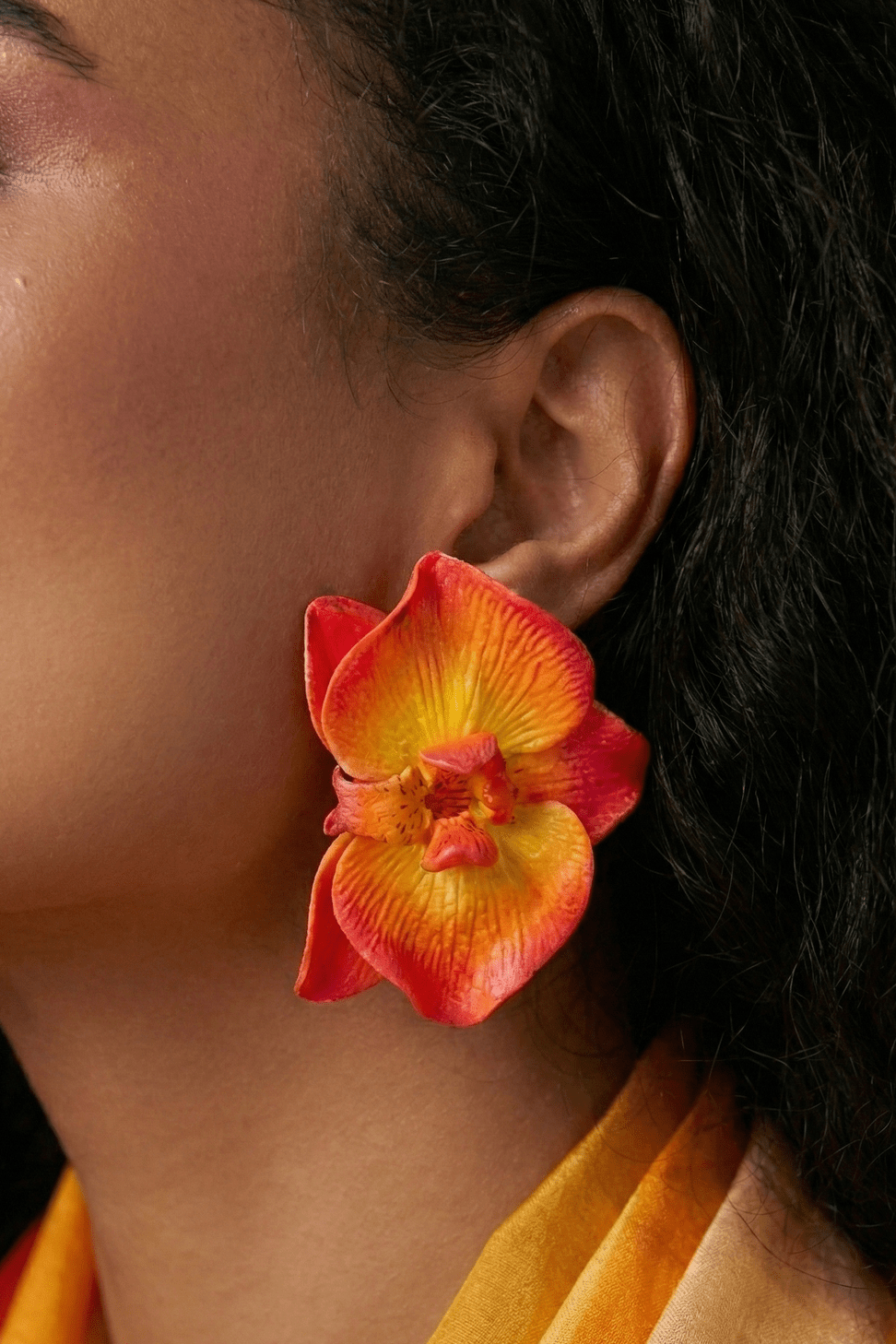 Close-up of handcrafted Sunset Orchid Earrings featuring sculpted orchid petals with red, orange, and golden yellow color blending.