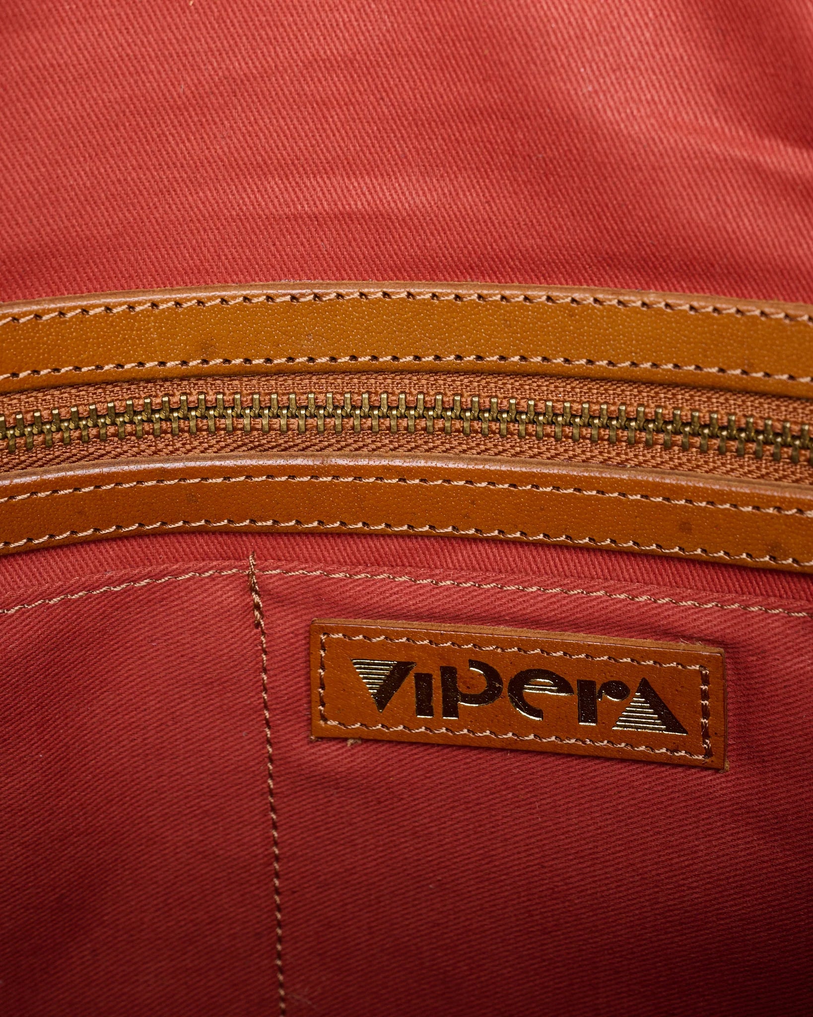 Interior detail of the Vipera Pillow Cognac handwoven leather bag showing the zippered pocket and branded leather logo patch.